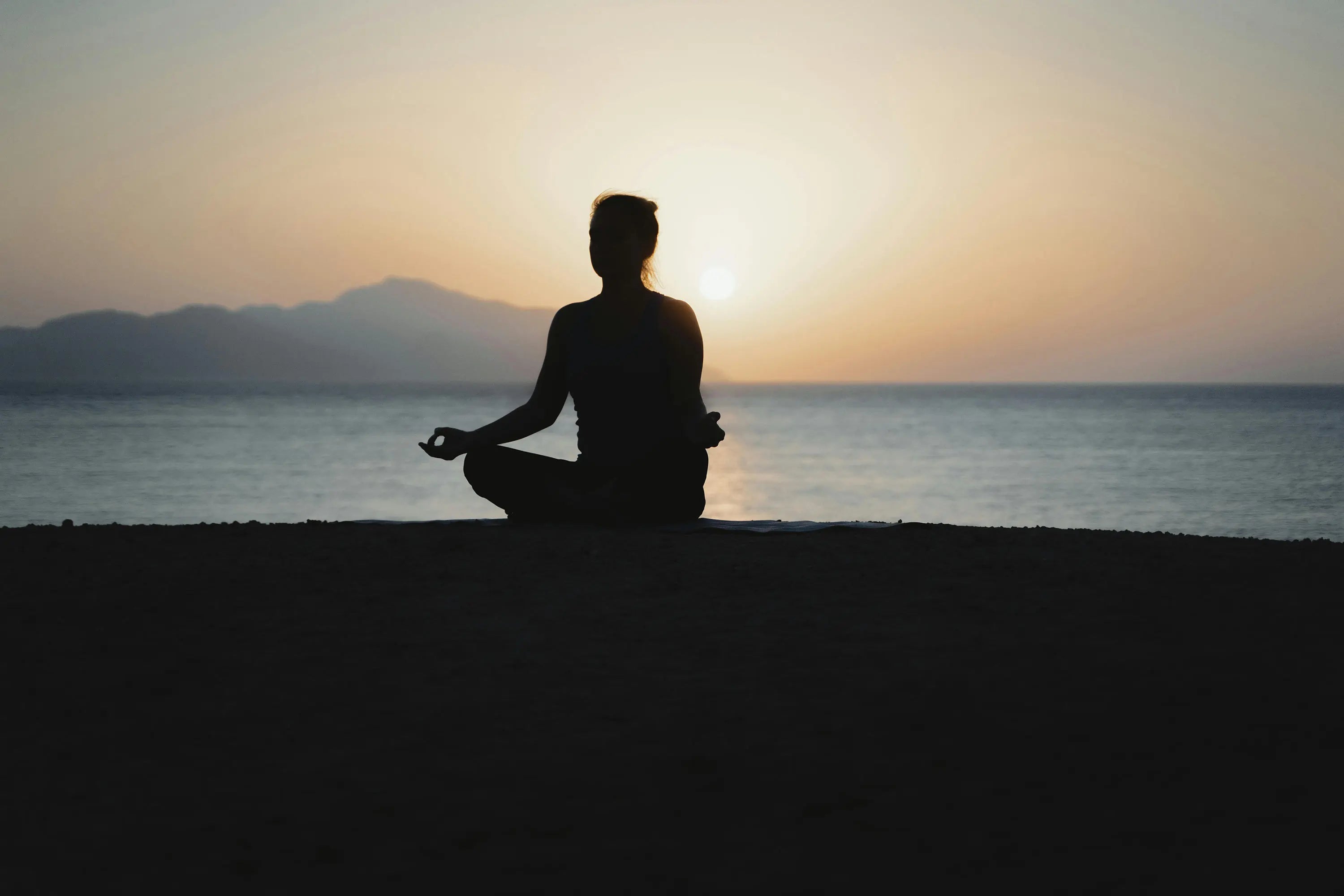 a silhouette of a person meditating on the beach