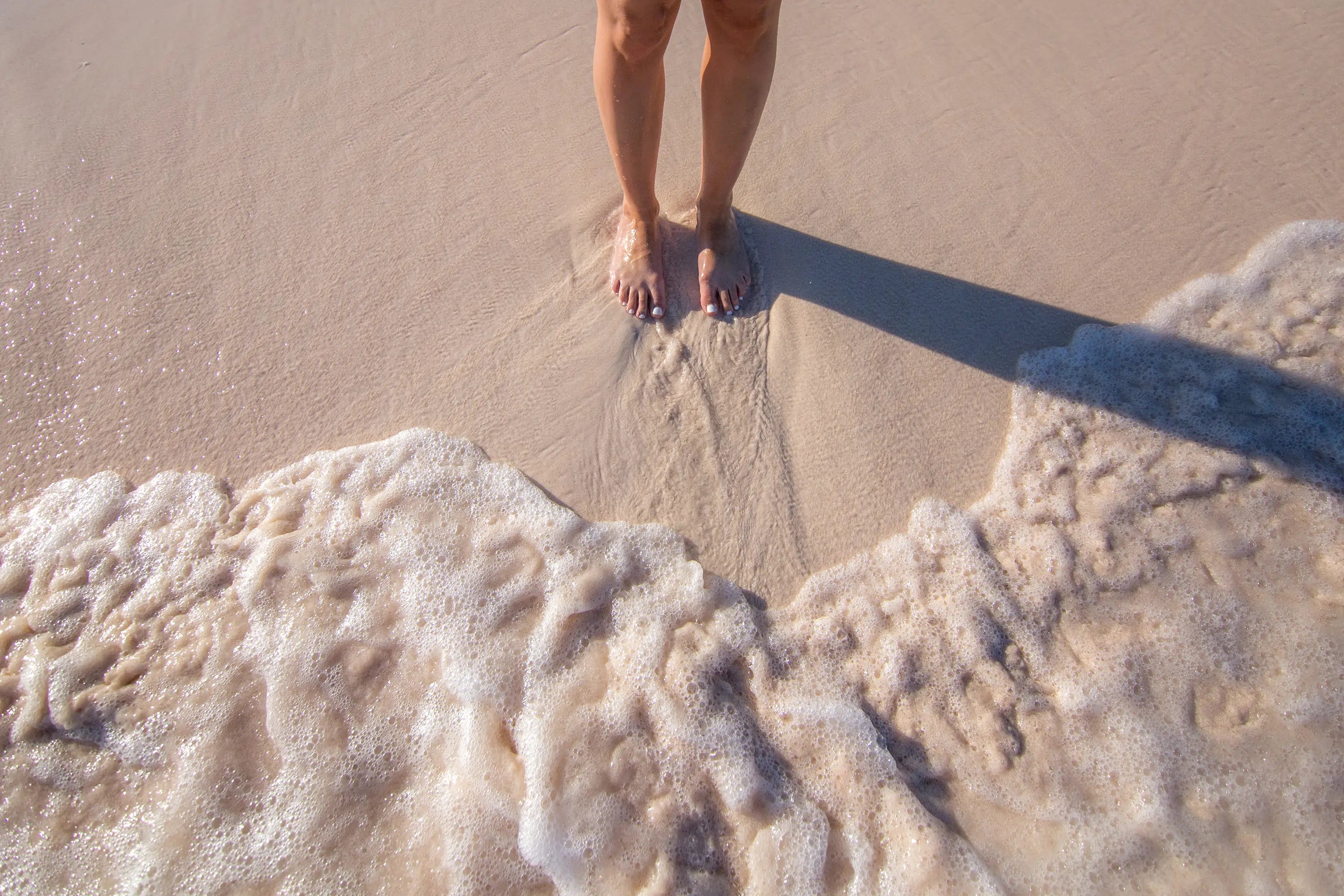 a woman standing barefoot on the beach