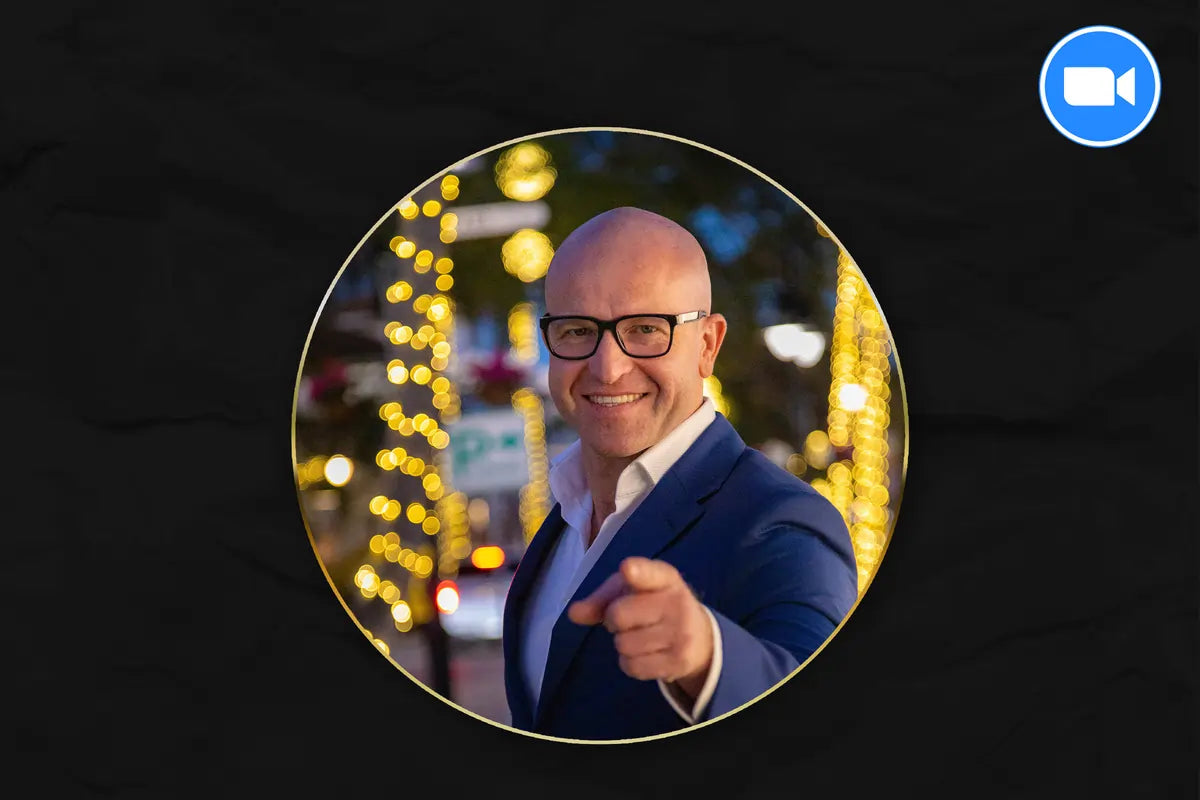 Man in a suit and glasses pointing forward with blurred lights in the background