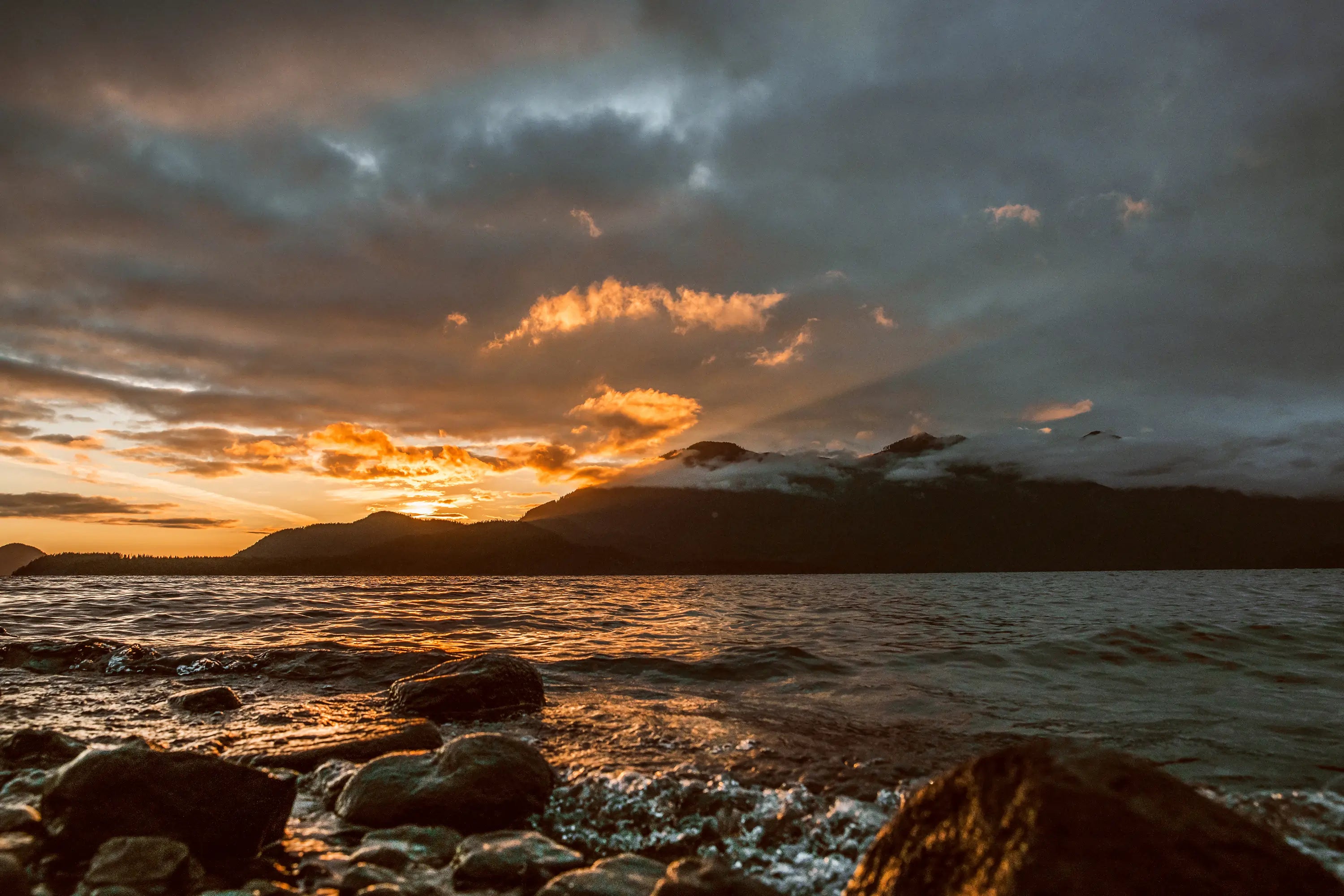 Sunrise over a mountain range with clouds over the ocean and rocks in the foreground